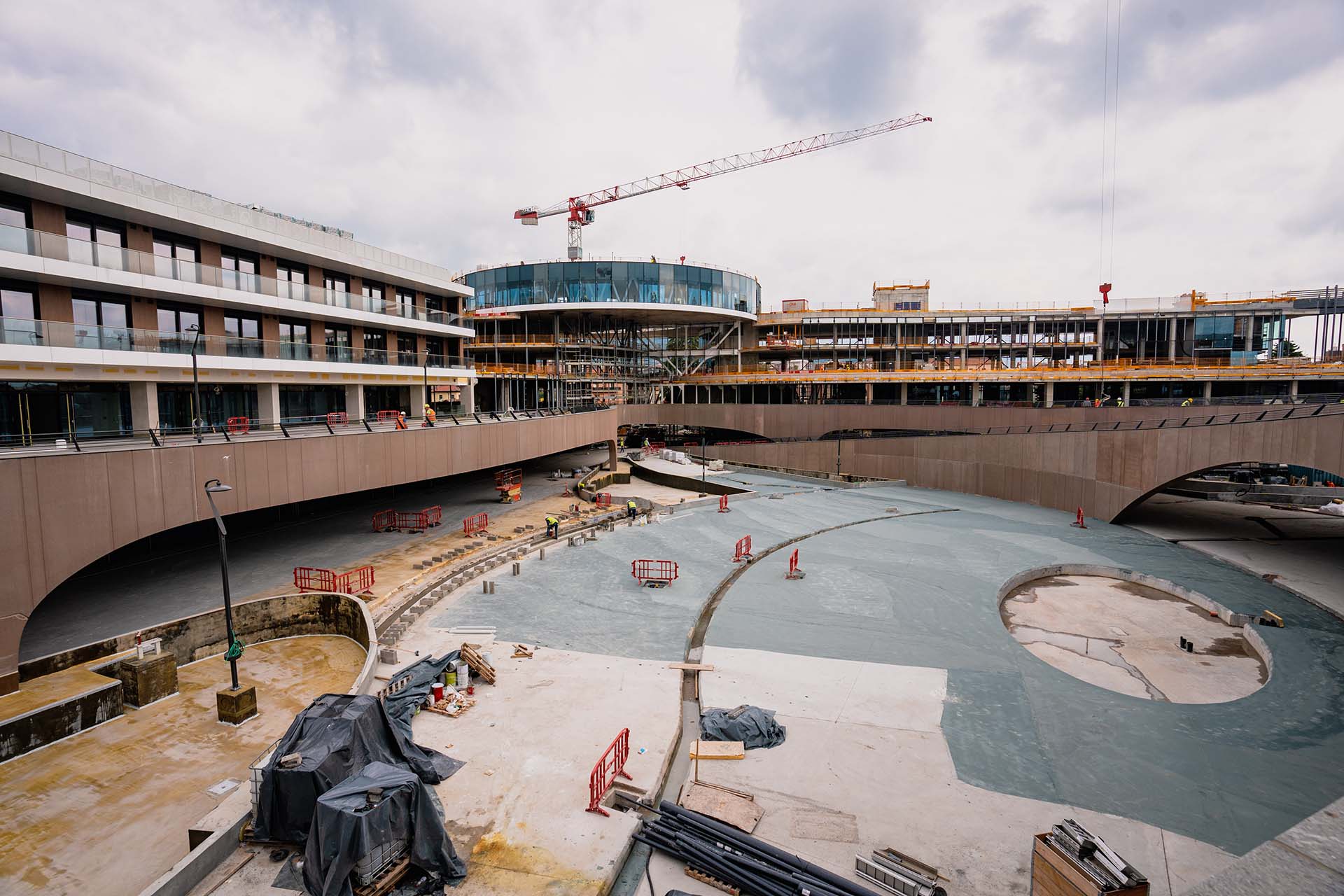 Dettaglio della realizzazione della pavimentazione della piazza del Sagittario che ospiterà la fontana, di fronte alle residenze. Sull’edificio retrostante destinato alla spa, Gualini comincia la vetrazione delle facciate (maggio 2024)